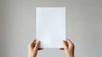 Hands holding blank white paper sheet against neutral background for mockup and branding projects.