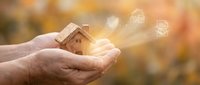 Hands holding wooden house model with glowing real estate icons, symbolizing property investment, home ownership, and digital housing market solutions.