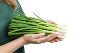 Fresh green onions held in hands against white background, ready for cooking and food preparation.