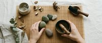 Hands holding wooden bowl with smooth stones on bamboo mat, spa wellness meditation setup with eucalyptus leaves and natural elements for relaxation.