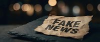 Torn paper with fake news text on dark surface with warm bokeh lights background representing misinformation and media literacy concepts.