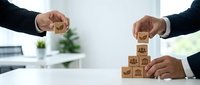 Business teamwork concept with hands building wooden blocks with icons representing growth, strategy and collaboration in modern office environment.
