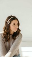 Young Caucasian woman with wavy brown hair wearing a stylish headband and cozy knit sweater, smiling softly in a bright minimal interior.