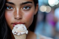 Young woman with freckles and natural makeup enjoying ice cream cone on blurred bokeh background, close up portrait showing genuine happiness and summer mood.