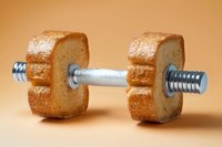 Creative food concept showing dumbbell made from sliced bread with metal bar. Fitness and diet metaphor on brown background.