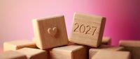 Wooden blocks stacked with heart symbol and 2027 date on pink background, representing new year planning, goals, and future aspirations for design projects.