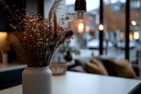 Cozy cafe interior with dried flowers in ceramic vase, pendant lights creating warm ambiance against blurred window background, modern minimalist decor setting.