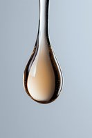 Macro shot of amber liquid drop with tiny air bubbles suspended in clear viscous substance against light gray background, showing surface tension and reflection.
