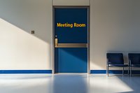 Blue door with meeting room text in corporate office hallway interior with empty chairs against white wall, dramatic diagonal shadow creates depth.