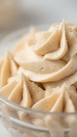 Creamy peanut butter frosting with smooth swirls in a glass bowl, ready for cake decorating, baking projects, and culinary applications.