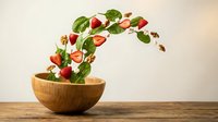 Fresh strawberries with green leaves and nuts flying from wooden bowl on table, dynamic food motion concept for healthy eating and organic nutrition.