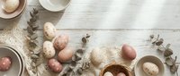 Elegant Easter table setting with pastel eggs, eucalyptus branches and ceramic dishes on rustic white wooden background for spring holiday celebrations.