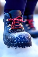 Winter hiking boot with red laces covered in fresh snow against blurred background, close-up macro photography showing texture and detail of footwear in cold weather.