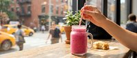 Person holding straw in pink smoothie drink at outdoor cafe table with city street view, urban lifestyle beverage concept for restaurants and food service marketing.