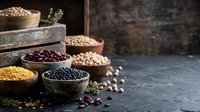 Assorted legumes and grains in bowls on dark surface, including lentils, chickpeas, beans and seeds for cooking, nutrition and healthy eating concepts.