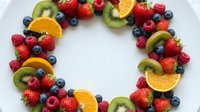 Fresh mixed fruit wreath with strawberries, blueberries, kiwi, orange slices and raspberries arranged in circle on white background for healthy eating concepts.