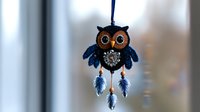 Decorative owl dreamcatcher with blue feathers and sparkly elements hanging against blurred background. Handmade ornament features crystal details and bohemian style.