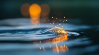 Glowing golden feather floating on rippling water surface creates magical reflection with bokeh lights and water drops at sunset. Ethereal nature photography.
