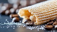 Fresh wafer roll sprinkled with powdered sugar surrounded by roasted coffee beans on dark background, macro food photography with selective focus.