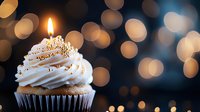 Single lit candle on white frosted cupcake against dark background with golden bokeh lights creating magical festive atmosphere for celebration and special occasions.