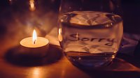 Glowing tealight candle beside a glass of water with sorry note, warm moody atmosphere symbolizing apology, forgiveness, and reconciliation.