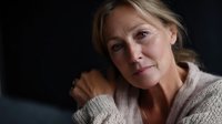 Mature blonde woman in cozy sweater with gentle smile and warm expression against dark background for lifestyle and wellness content.