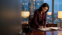 Professional businesswoman working late at office desk with city lights background, corporate executive reviewing documents in modern workplace.