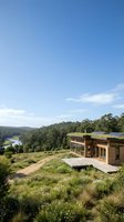 Modern sustainable eco house with solar panels nestled in natural landscape overlooking valley and forest under clear blue sky for green living concepts.