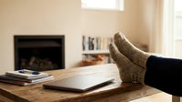 Person relaxing with feet up on wooden table wearing cozy knit socks in warm living room with fireplace and books creating comfortable home atmosphere.