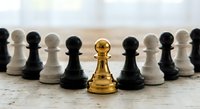 Golden chess pawn standing out among black and white pawns on wooden surface, symbolizing leadership, uniqueness and strategic thinking in business.