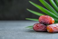 Fresh dates fruit with palm leaves on stone surface for healthy eating and Middle Eastern cuisine concepts.