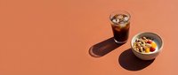 Cold cola drink with ice cubes and bowl of cereal with milk on coral background, flat lay composition for food and beverage advertising.