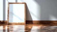 Empty wooden picture frame leaning against white wall on hardwood floor with dramatic window light and shadows creating minimalist interior scene.
