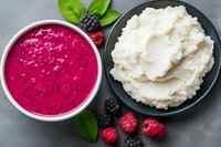 Fresh raspberry and blackberry smoothie bowl with creamy coconut yogurt served with green basil leaves on gray stone background, healthy breakfast.