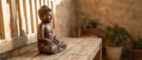 Bronze Buddha statue in meditation pose on wooden bench with warm sunlight creating peaceful zen atmosphere for mindfulness and spiritual practices.