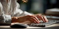 Professional woman hands typing on laptop keyboard in modern office workspace with natural lighting for business productivity.
