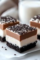 Layered dessert bar with chocolate cookie base, creamy white filling, milk chocolate top layer garnished with chocolate sprinkles, served on parchment paper.