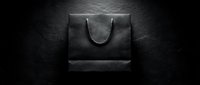 Black shopping bag with handles on dark textured background, suitable for retail, luxury branding, e-commerce, and packaging design projects.
