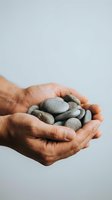 Adult male hands holding smooth river stones against neutral background, representing care, wellness, mindfulness and natural healing practices.