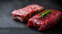 Raw beef steaks with fresh rosemary sprig on dark stone background, selective focus on juicy red meat cuts showing marbling and texture for food photography.