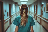 Female medical worker in scrubs walking down empty hospital corridor, view from behind with long blonde hair in half-up style, moody teal atmosphere.