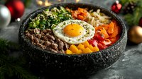 Korean bibimbap bowl with sunny side up egg, beef, vegetables, rice and spicy sauce served in stone bowl on dark background with Christmas decorations.