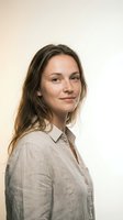 Young Caucasian woman with freckles in beige linen shirt smiling confidently against neutral background for professional headshot and business portrait.