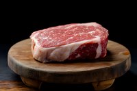 Raw marbled beef steak on round wooden cutting board against dark background, fresh premium meat cut with white fat marbling pattern.