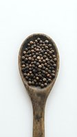 Wooden spoon filled with black peppercorns isolated on white background for culinary and cooking designs.