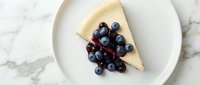Slice of creamy cheesecake topped with fresh blueberries and cherries on white plate, marble background for dessert menu and bakery advertising.