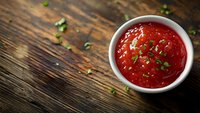 Fresh red tomato sauce garnished with chopped herbs in white ceramic bowl on rustic wooden table background, selective focus with copy space.