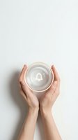 Female hands gently holding empty glass bowl from above on white background. Minimalist kitchen concept for cooking, baking and food preparation.