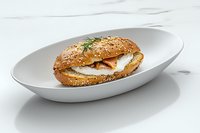Fresh fried egg sandwich on multigrain bagel with herbs and sesame seeds served on white oval plate against marble background for food service menu.