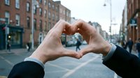 Two hands forming a heart shape together on a city street, symbolizing love, unity, and connection in an urban setting.